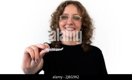 Kaukasische junge Frau zeigt einen unsichtbaren Silikon-Aligner für die Zahnkorrektur. Weibliche Hand hält die Kunststoffspangen Zahnheilkunde Halter zu strai Stockfoto