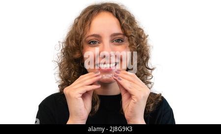 Lächelnde Frau, die ihren unsichtbaren Silikon-Aligner zur Zahnkorrektur aufsetzt. Mobiles Konzept der kieferorthopädischen und zahnmedizinischen Versorgung. Stockfoto