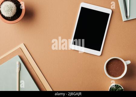 Teil des Arbeitsplatzes eines modernen Designers mit Tablet, Tasse Kaffee, Notizbuch mit Stift auf der Oberseite, Pflanzen in Blumentöpfen und Bleistiften auf dem Copybook Stockfoto