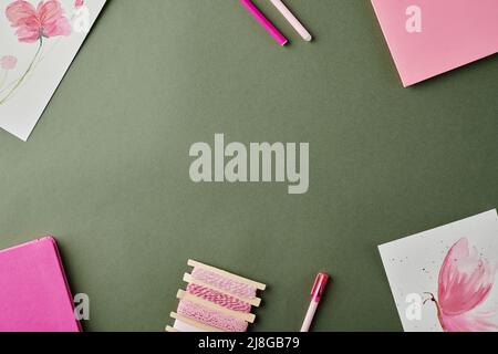 Gruppe von rosa Notizbüchern, Textmarkern, Feder- und Aquarellzeichnungen von Blumen und Schmetterlingen auf einem grauen Tisch mit Copyspace in der Mitte Stockfoto