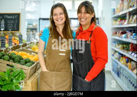 Fröhliche hispanische Verkäufer in Schürzen im Supermarkt Stockfoto