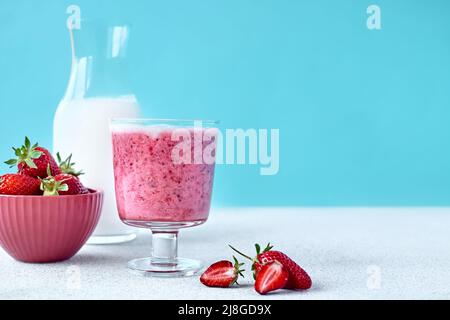 Erdbeer-Kokosnuss-Milchshake, Frappé oder Smoothie im Trinkglas auf hellblauem Hintergrund. Gesunde vegane Ernährung erfrischendes Getränk. Gesunde Ernährung und dri Stockfoto