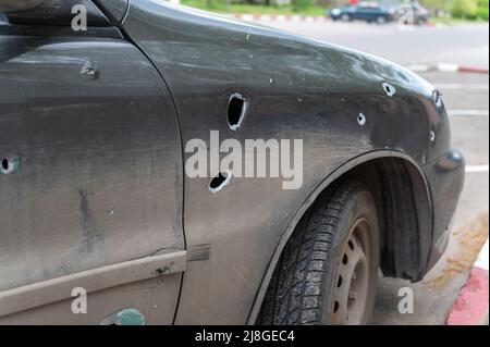 Ein PKW mit Durchgangslöchern aus Schrapnel, der auf dem Parkplatz steht. Beschädigte Limousine während des Krieges in der Ukraine. Konsequenzen des Beschuss von Stockfoto