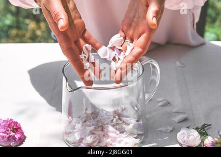 Frau bereitet Rosenwasser mit rosa Rosenblüten in einer Glasschüssel zu. Hautpflege und Spa, natürliche Schönheitsbehandlungen, hausgemachte Kosmetik. Stockfoto