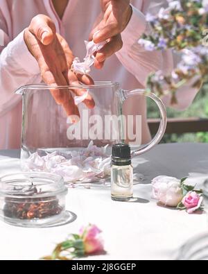 Frau bereitet Rosenwasser mit rosa Rosenblüten in einer Glasschüssel zu. Hautpflege und Spa, natürliche Schönheitsbehandlungen, hausgemachte Kosmetik. Stockfoto