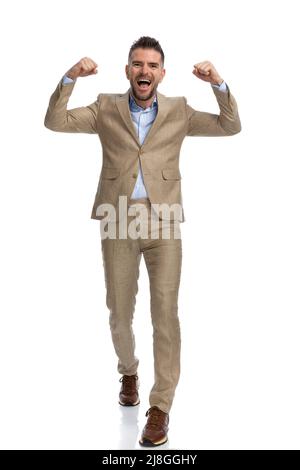 Champion Geschäftsmann mit Waffen in der Luft zu Fuß, schreiend und feiert den Sieg auf weißem Hintergrund im Studio Stockfoto