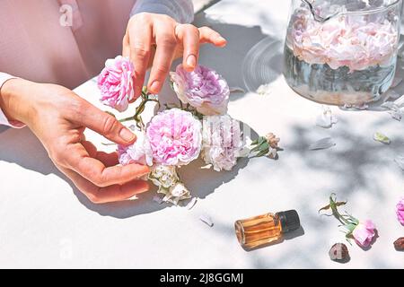 Frau bereitet Rosenwasser mit rosa Rosenblüten in einer Glasschüssel zu. Hautpflege und Spa, natürliche Schönheitsbehandlungen, hausgemachte Kosmetik. Selektiver Fokus. Stockfoto