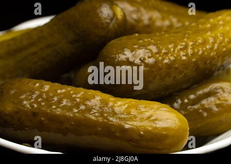 Nahaufnahme von gesalzenen, eingelegten Gurken auf einem weißen Teller auf schwarzem Hintergrund Stockfoto