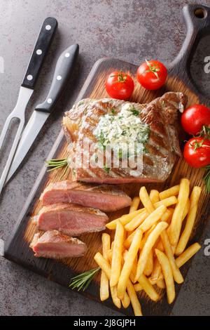 Saftige Steaks für Sommer und Grill, mit pommes frites, Kräuterbutter in der Nähe auf dem Holzbrett auf dem Tisch. Vertikale Draufsicht von oben Stockfoto