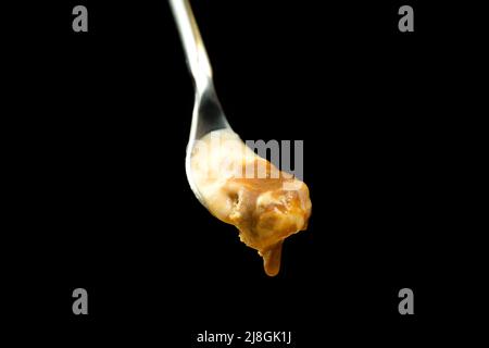 Makrofoto eines Dessertlöffels mit Karamell-Eis vor einem schwarzen Hintergrund mit Kopierfläche. Stockfoto