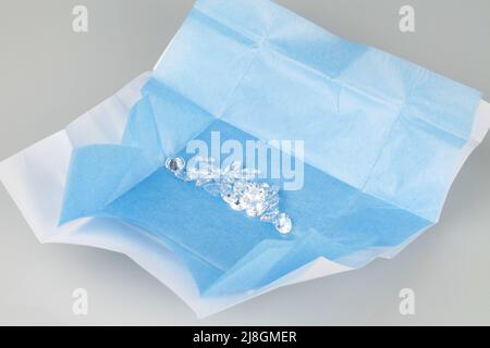 Offenes Paket loser Diamanten mit blauem Papierhintergrund. Verschiedene Diamantgrößen. Stockfoto