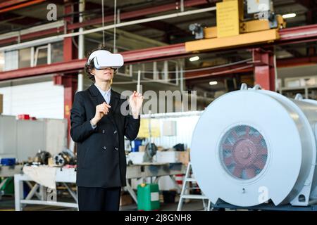 Junge Arbeiterin der modernen Fabrik in vr Headset, die Präsentation des virtuellen Produkts in der Werkstatt oder im Lager Stockfoto