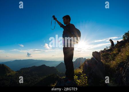 Der Fotograf, der auf einem Bergvorsprung steht und den wunderschönen Sonnenuntergang vor einer blauen Himmelswolke genießt, Doi Chiang Daw, Thailand Stockfoto