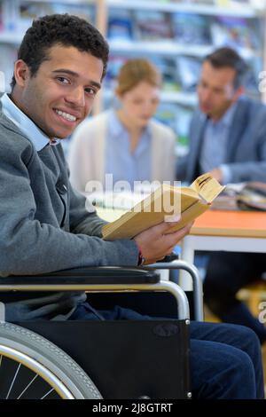 Lächelnder körperlich behinderter Mann im Rollstuhl mit Buch Stockfoto