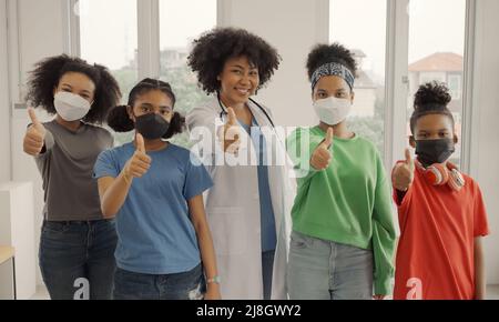 Afroamerikanischer Arzt und Kinder mit Maske glücklich Daumen nach oben Finger im Krankenhaus oder in der Klinik. Stockfoto