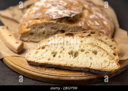 Weiße Brotscheiben und Messer. Ein Laib Brot mit der ersten Hälfte bereits geschnitten. Drei Scheiben Brotscheiben. Stockfoto