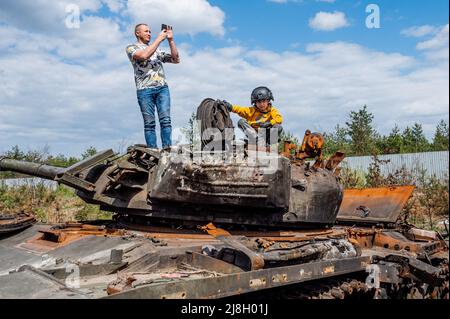 Nalyvaikivka, Ukraine. 15.. Mai 2022. Ein Mann, der ein Foto gemacht hat, und ein Kind, das auf einem zerstörten russischen Panzer in Nalyvaikivka sitzt. Kredit: SOPA Images Limited/Alamy Live Nachrichten Stockfoto