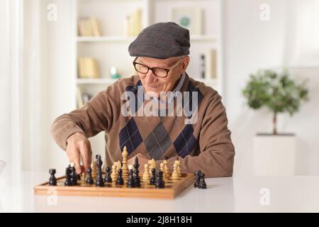 Älterer Mann, der zu Hause sitzt und Schach spielt Stockfoto