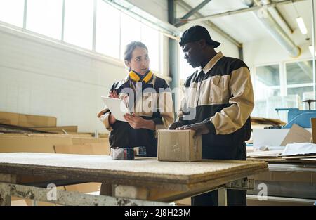 Zwei Kollegen in Uniform mit Tablet-pc und diskutieren den Transport verpackter Produkte, während sie im Lagerraum stehen Stockfoto