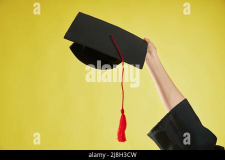 Vorderansicht des weiblichen Handhebens, Halten, zeigt das Mortarboard. Mädchen in einem Abendkleid, das an der Hochschule, Universität oder Hochschule abschloss. Isoliert Stockfoto