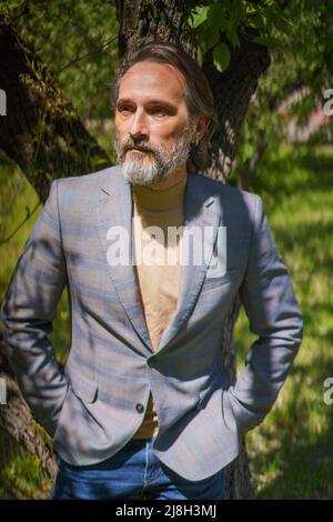 Reifer, gutaussehender Mann im Jahr 40s 50s in einem Park oder Hof, weg vom Geschäft oder eine Pause im warmen Frühlingsgarten im Freien. Schöner graubärtiger Geschäftsmann im Freien. Stockfoto