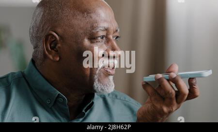 Reife grauhaarige 60s biracial Mann mit Bart afroamerikanischen Senior alten Mann zu Hause halten Smartphone sprechen Telefon Mikrofon Lautsprecher Audio Voice Stockfoto