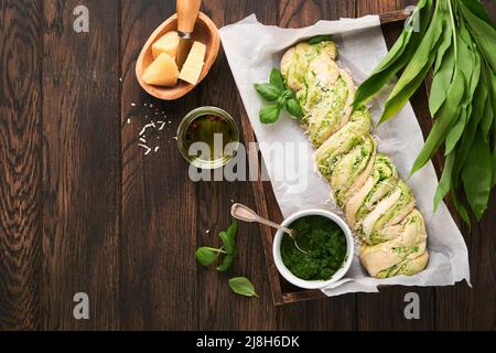 Geflochtenes Bärlauch-Pesto Brioche. Hausgemachtes frisches Pull-Apart-Brot mit Bärlauch-Pesto auf Holzbrett auf Holzhintergrundtisch. Italienisches Brot. C Stockfoto