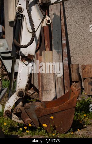 Ein Eimer wird am Ende seines Arms auf einem Hydraulikzylinder auf den Boden gelegt. Stockfoto