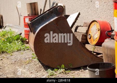 Ein rostiger Eimer liegt auf dem Boden, ringsum sind rote und gelbe Öl- und Benzinkannen. Stockfoto