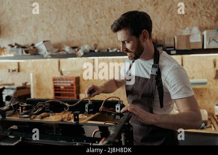 Lächelnder junger Mann, der in einer Werkstatt die Kaffeemaschine repariert Stockfoto