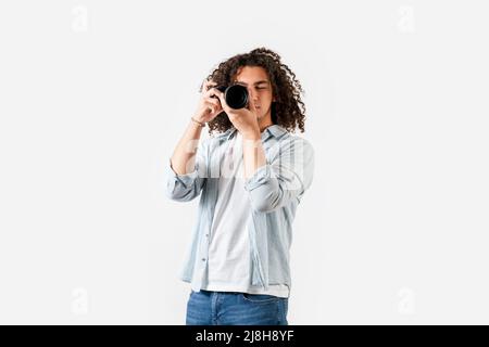 Der junge Mann mit lockigen Haaren schießt mit der Kamera an der Hand. Hobby und Fotografie Konzept. Hochwertige Fotos Stockfoto
