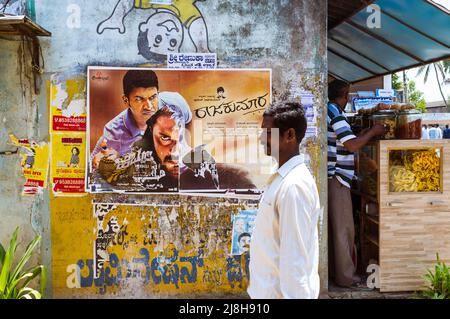 Belur, Karnataka, Indien : Ein Mann geht an einem Bollywood-Filmplakat an einer Wand vorbei. Stockfoto