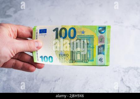 Hand halten und geben hundert 100-Euro-Banknoten. Geld in Menschenhand auf grauem Hintergrund Stockfoto