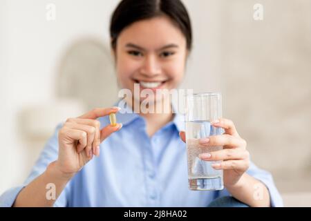 Fröhliche asiatische Frau mit einem Glas Wasser und einer Pille Stockfoto