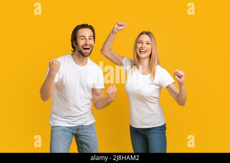 Zufriedener junger kaukasischer Ehemann und blonde Frau im weißen T-Shirt freuen sich über den Sieg, sehr viel Stockfoto