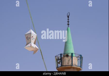 Hängende Ramadan-Laternen-Straßendekorationen mit dem Minarett einer Moschee im Hintergrund vor einem blauen Himmel in Jordanien im Nahen Osten Stockfoto