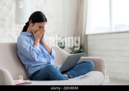 Verärgert asiatische Frau mit Notebook auf dem Schoß weinen Stockfoto