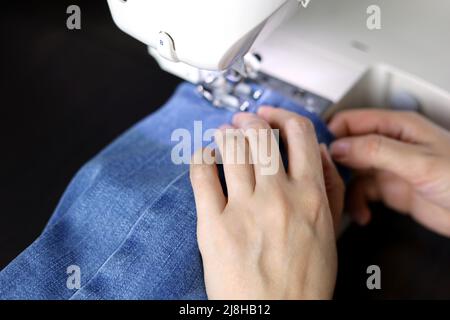 Frau, die an der Nähmaschine arbeitet, weibliche Hände aus der Nähe. Näherin näht Jeans, Konzept der Ausbesserung von Kleidung Stockfoto