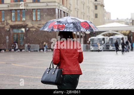 Heftiger Regen in einer Stadt, Frau in roter Lederjacke und schwarzem Rock mit Regenschirm, die auf dem Hintergrund der Menschen die Straße entlang läuft Stockfoto