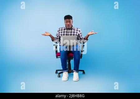 Überrascht junger schwarzer Mann, der auf den Laptop-Bildschirm schaut, Fehler im Geschäftsprojekt macht, fehlende Frist, blauer Hintergrund Stockfoto