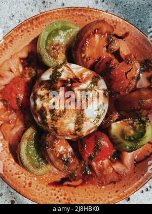 Burrata-Käse mit Tomaten. Salat in Sommersonnenlicht. Stockfoto
