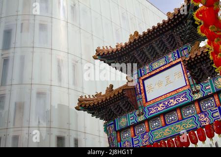 Das Chinatown-Tor im Stil der Qing-Dynastie der Grand Eingang zu Chinatown, London, Großbritannien, steht im Kontrast zum modernen W London Hotel mit Glasfront Stockfoto