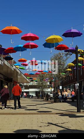 Über einer Fußgängerstraße im Zentrum von Alfreton in Derbyshire wurde ein farbenfrohes Display mit Regenschirmen installiert. Stockfoto