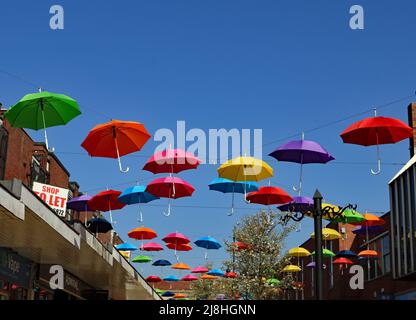 Über einer Fußgängerstraße im Einkaufszentrum von Alfreton in Derbyshire wurde ein farbenfrohes Display mit Regenschirmen installiert. Stockfoto