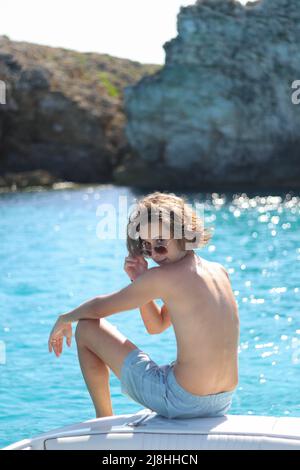 Kleiner Junge genießt die Freiheit auf Luxus-Yacht-Deck im Wind entspannen auf High-End-Boot Sommerurlaub Reise. Lange blonde Haare und sonnengebräunten Körper. Stockfoto