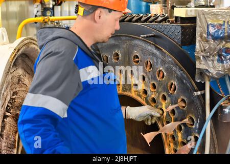 Ein Helmingenieur inspiziert und repariert die Gasanlagen im Kesselraum. Reinigung und Wartung des industriellen Dampfkessels. Stockfoto