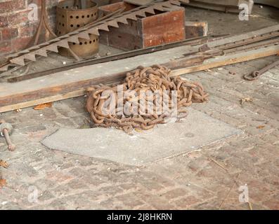 Stapel alter rostiger Ketten auf einem Werkstattboden Stockfoto