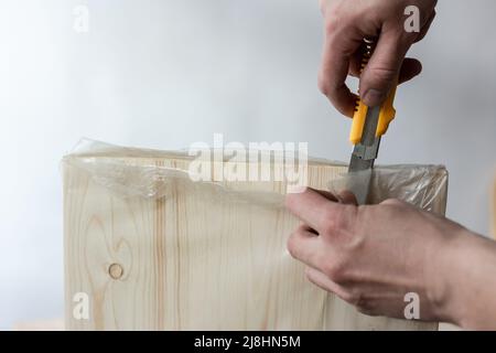 Auspacken eines Möbelbretts mit einem Messer. Auspacken eines Holzbretts. Stockfoto
