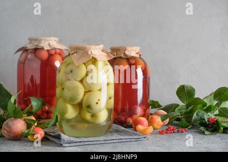 Drei hausgemachte Dosenfrüchte, Apfel- und Kirschkompott in großen Gläsern auf einem grauen Tisch. Stockfoto