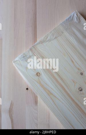 Möbelbrett in Zellophan-Verpackung auf Holzhintergrund. Holzdiele. Stockfoto